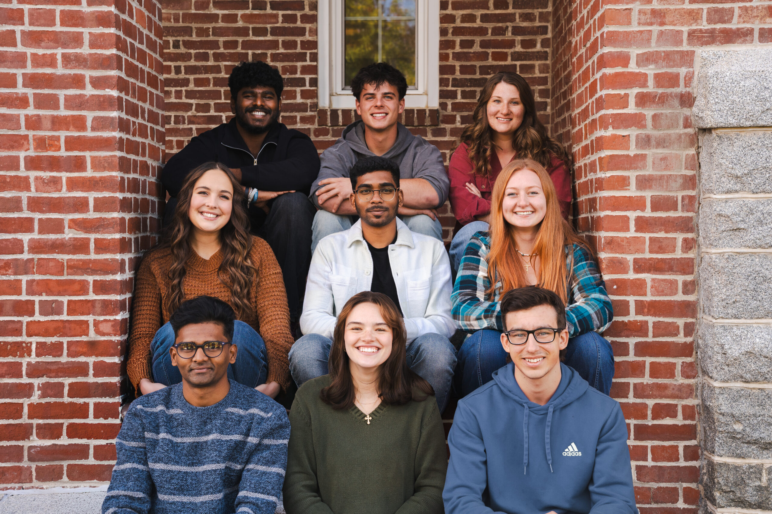 Three young people sitting on grass in front of a building, enjoying each other's company.